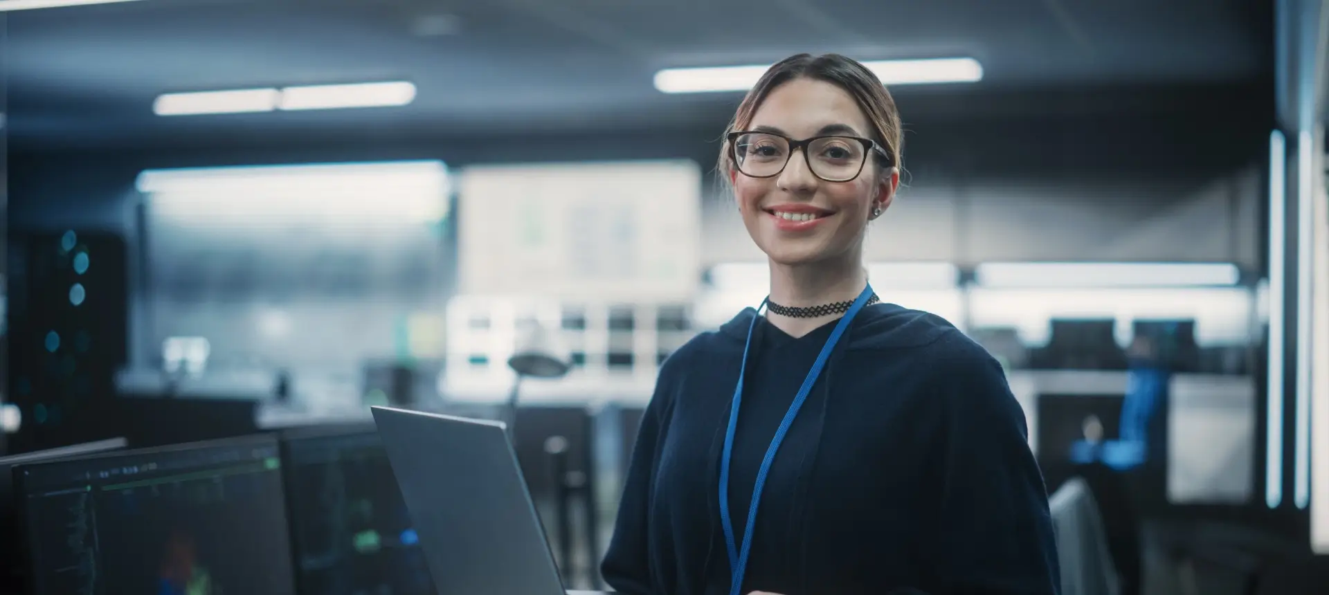 Smiling woman with laptop in tech office.